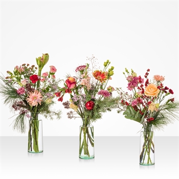 Three glass vases with assorted pink, orange, and red flowers arranged on a white surface.