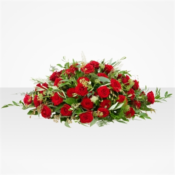 Horizontal arrangement of red roses with greenery on a pale background (funeral casket spray)