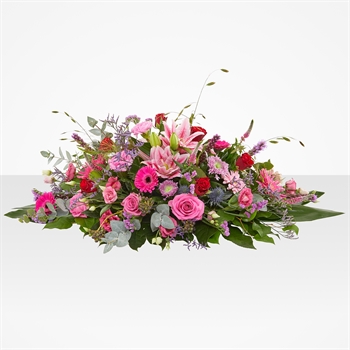 Colorful floral centerpiece featuring pink roses, purple daisies, and greenery on a white background.